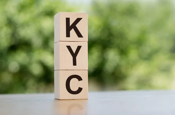 The word KYC - Know Your Customer, built from wooden cubes outdoors on the background of nature.
