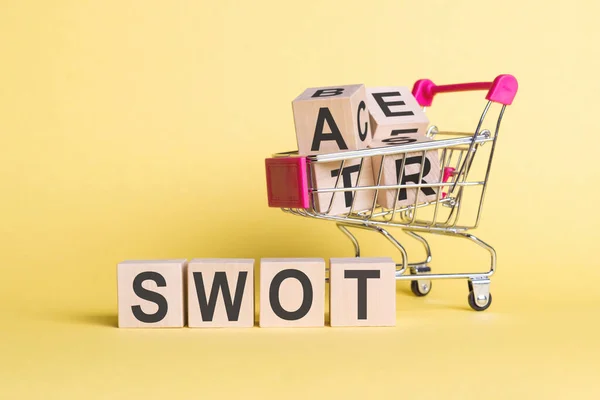 Das Wort Swot Auf Holzwürfeln Auf Gelbem Hintergrund Mit Einkaufswagen — Stockfoto