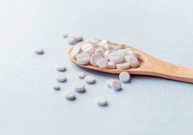 Açık mavi arka plandaki tahta kaşıkta beyaz ilaç ve tablet çeşitleri. Sağlık hizmeti kavramı.