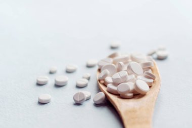 Açık mavi arka planda yuvarlak tabletli tahta kaşık izole edilmiş. Haplar ve uyuşturucular.