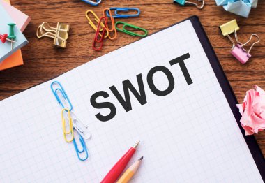 Masada renkli ataçlar ve buruşuk kağıtlarla SWOT metni olan not defteri.