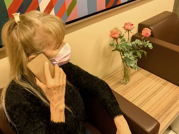 Yetişkin sarışın kadın pembe cerrahi akıllı telefon kemeriyle konuşuyor. Bir buket gülün yanında..