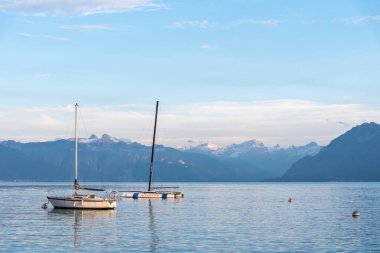 Karlı tepelerle çevrili iki teknesi olan sakin mavi sularıyla Alp Gölü. Cenevre Gölü 'ndeki Montreux