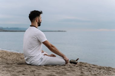 Şafakta sahilde meditasyon yapan bir adam.