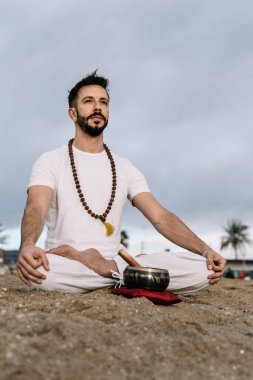 Sakallı, beyaz bir adam şafak vakti sahilde meditasyon egzersizi yapıyor.