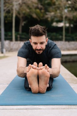 Sakallı bir adam parkta yoga egzersizleri yapıyor.
