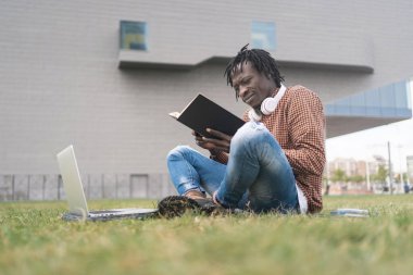 Afrika Üniversitesi öğrencisi bir kitap okuyor ve açık hava kampüsünde öğreniyor.