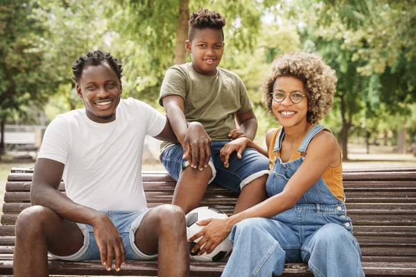 Portrett av lykkelig afroamerikansk familie med unge, kule foreldre og søte, smilende barn som sitter på benken i offentlige parker – stockfoto