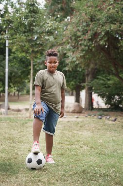 Futbol topuyla parkta egzersiz yapan Afro-Amerikan çocuğun portresi.