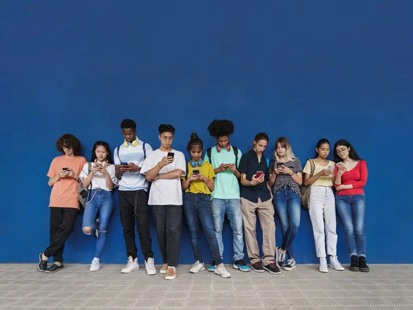 Ryhmä monirotuisia teini-ikäisiä opiskelijoita katsomassa älypuhelimia lukiotauolla - Sosiaalisen median käsite Uuden sukupolven ongelma — kuvapankkivalokuva