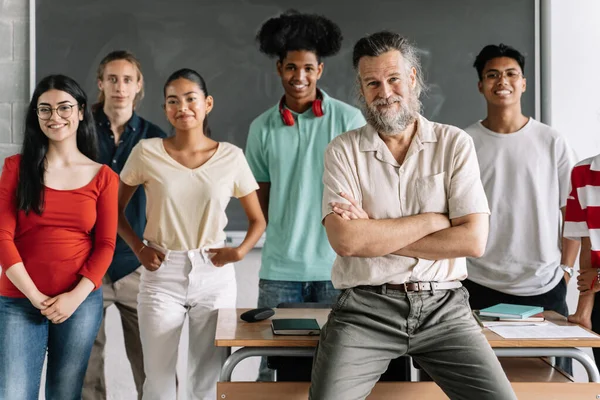 Multi-rasegruppe av ungdomsskoleelever og vennlig seniorlærer med skjegg i klasserommet på videregående skole. Kulturelt mangfold i utdanningen – stockfoto