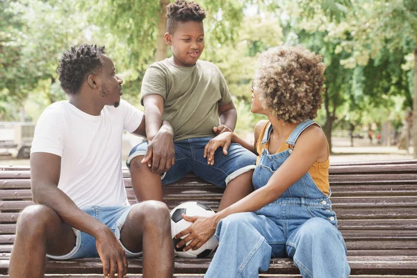 Afrikkalainen amerikkalainen perhe nuori viileä tuhatvuotinen vanhemmat ja söpö lapsi istuu penkillä ulkona julkinen puisto — kuvapankkivalokuva