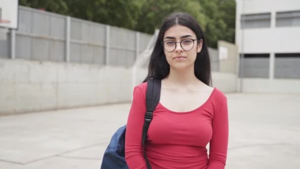 Retrato de Jovem Hispânica Estudante Colégio Feminino com cabelos escuros, óculos e roupas casuais vermelhas no quintal da Escola Secundária — Vídeo de Stock