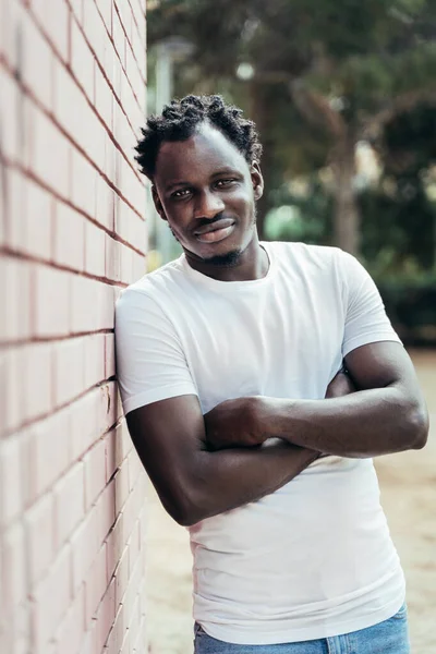 Portrait of Handsome young African man with crossed arms leaning on brick wall — Stock Photo, Image