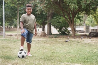 Futbol topuyla parkta egzersiz yapan Afrikalı Amerikalı hafif kilolu bir çocuk. hafif kilolu küçük çocuk.