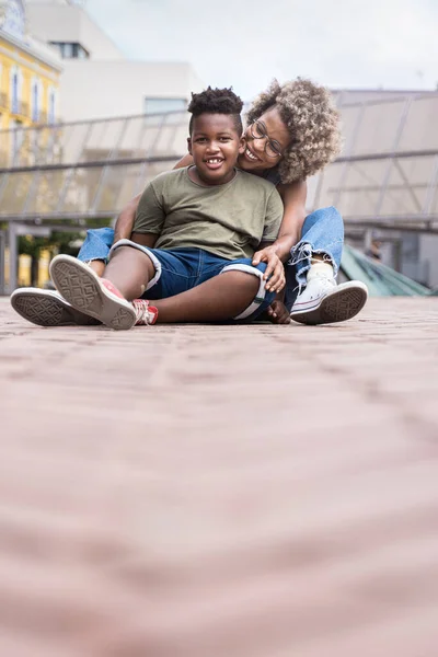 Afroamerikansk elskov Mamma og Sønn sitter utendørs i byen i en vakker mødredag på – stockfoto