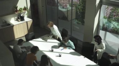 Modern gündelik giysiler içindeki çok ırklı genç meslektaşların üst düzey görüşü iş toplantısına gelip şık bir ofiste masanın etrafında oturmaları.