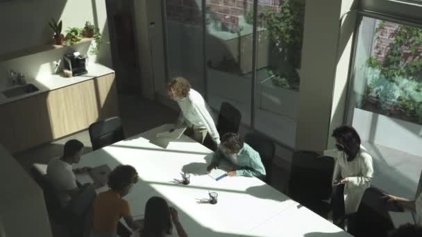 Vue de dessus de plusieurs jeunes collègues ethniques en tenue décontractée moderne arrivant à une réunion d'affaires et assis autour de la table dans un bureau élégant — Video