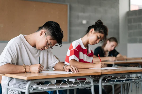 Aasialainen opiskelija kirjallisesti tentti college lukion luokkahuoneessa - Multi Etninen teini luokkatoverit keskittyminen tekee testi — kuvapankkivalokuva