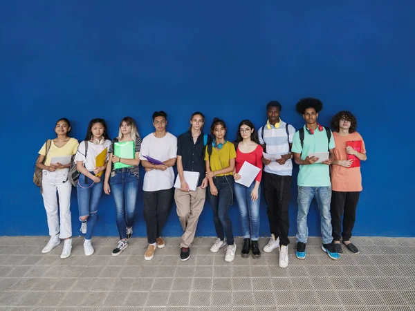 Ryhmä monirotuisia teiniopiskelijoita katselemassa kameraa sinisen muurin yllä. Teini monikansallinen luokkatoverit ystävät koulutuksen monimuotoisuus — kuvapankkivalokuva