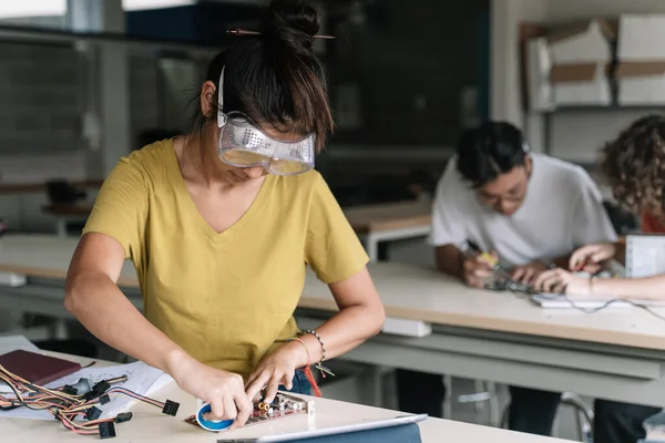 Tenåringsstudent ved Asias videregående skole med vernebriller som arbeider med elektroniske kretskort i vitenskapsteknologiverkstedet - digital innovasjon i utdanningen – stockfoto