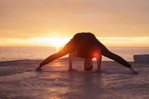 Ung mann som gjør avanserte yogaøvelser nær havet ved soloppgang Sunn yoga-rutine – stockfoto
