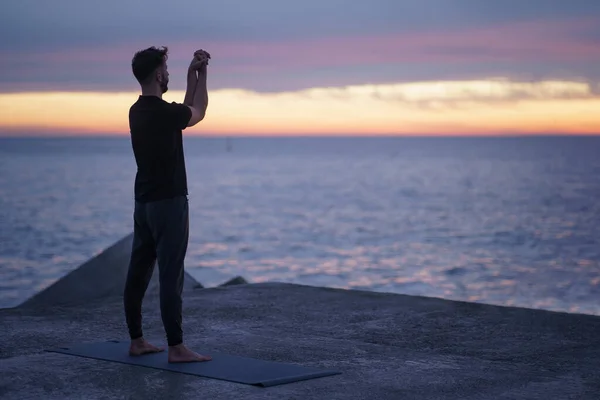 Mann-silhuett som gjør yoga øvelser foran havet ved soloppgang - Spirituell og sunn yoga-rutine – stockfoto