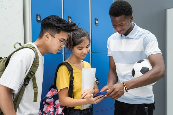 Monirotuinen teini opiskelija ystävät jakavat sosiaalisen median älypuhelin yläasteen kaappi käytävällä — kuvapankkivalokuva