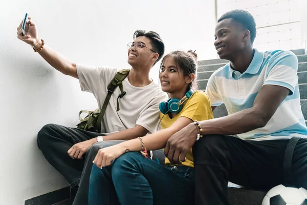 Asiatiske og afrikanske collegevenner som tar bilde selfie med smarttelefon i trappa på videregående skole – stockfoto