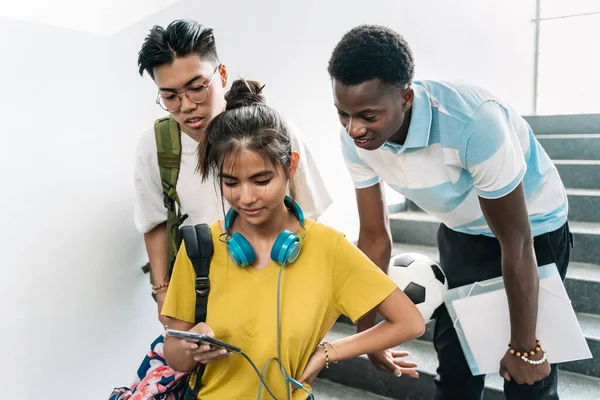 Multi etniske asiatiske og afrikanske tenåringsstudenter som deler sosiale medier på smarttelefon på videregående skole – stockfoto