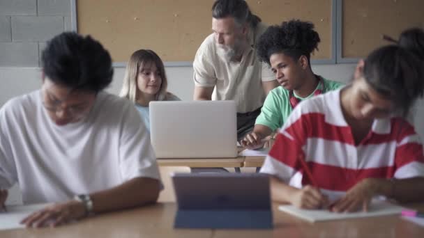 Profesor de asistencia a estudiantes multiétnicos en el aula de la escuela secundaria moderna. Amistoso Maestro con barba explicando la tarea. Computadoras portátiles y nuevas tecnologías en la educación — Vídeos de Stock