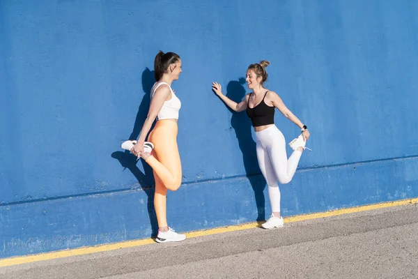 Twee vrouwelijke vrienden samen aan het trainen doen stretching workout over blauwe buitenmuur — Stockfoto