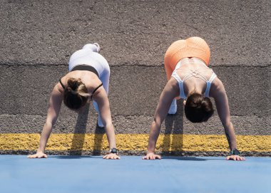 İki kadın mavi duvara karşı esneme egzersizi yapıyor. Bayan arkadaşlar sabahları birlikte dışarıda egzersiz yapıyorlar.