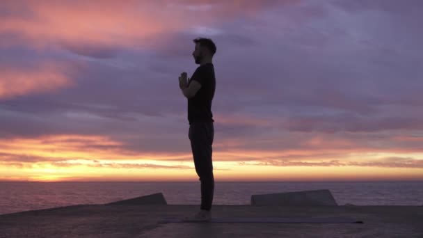 Jonge atletische man die yoga poseert voor de oceaan bij zonsopgang. Gezonde geestelijke ochtendyoga routine — Stockvideo