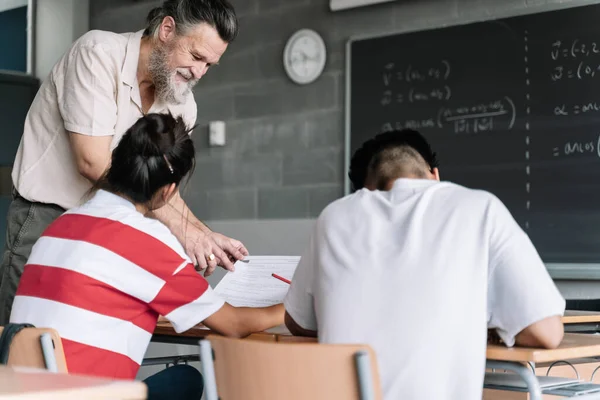 Moden professor som forklarer matematikk for tenåringsstudenter. Vennlig lærer med skjegg hjelper student i klasserom – stockfoto