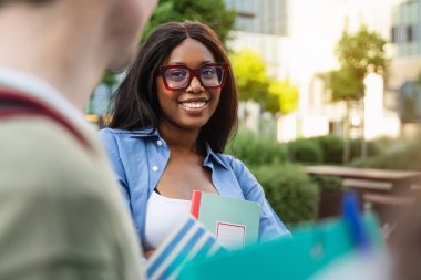 Gözlüklü siyah kız öğrenci ve grup arkadaşları üniversite binasının önünde buluşuyorlar.