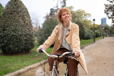 Güler yüzlü bir kadın güz gününde bisiklet sürüyor.