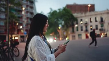 Genç Asyalı kadın, şehirde gece sokakta yürürken cep telefonu kullanıyor, harita uygulamasında yön arıyor