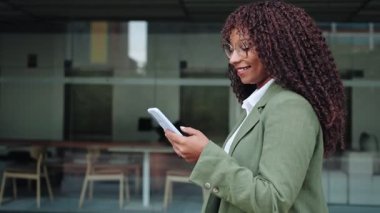 Kıvırcık saçlı, cep telefonu kullanan genç bir iş kadını işe gidiyor.