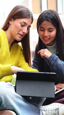 Tablet kullanan iki genç kadın, okul ödevleri üzerinde birlikte çalışıyorlar.