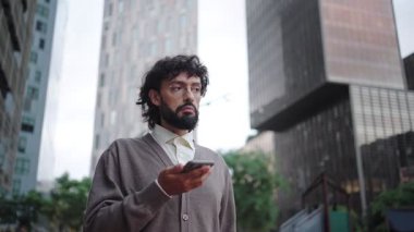 Modern bir şehirde açık havada akıllı telefon kullanan İspanyol asıllı profesyonel bir adam.