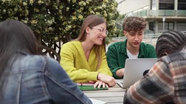 Sınavlar için dizüstü bilgisayar kullanan öğrenciler üniversite kampüs parkında oturuyorlar.