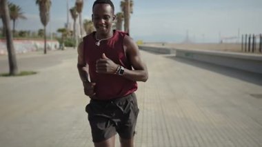 Genç Afrikalı adam plaja yakın koşuyor ve maraton koşusuna hazırlanıyor.