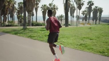 Sahilin yakınındaki bir şehir parkında koşan Afrikalı Amerikalı bir adam, sabah antrenmanı yapıyor.