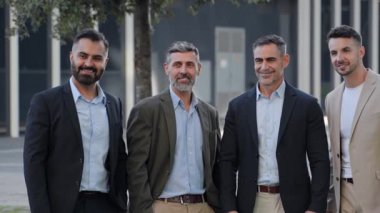 Bir ofis binasının önünde duran dört işadamı başarılı bir anlaşmadan sonra gülümsüyor.