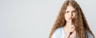 Kıvırcık uzun saçlı, günlük kıyafetler giymiş, işaret parmağını dudaklarında tutan, 