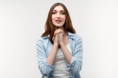 Uzun düz saçlı esmer bir kadın, günlük kıyafetler giymiş, çenesinin yanında ellerini birarada tutuyor, nazikçe gülümsüyor, sevimli bir yüz ifadesi var. İnsani duygular, yüz ifadesi kavramı.