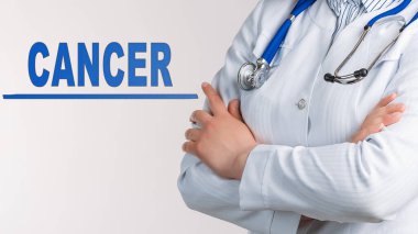 Beyaz arka planda kelime kanseri. Yakınlarda beyaz önlüklü ve steteskoplu bir doktor var. Tıbbi konsept