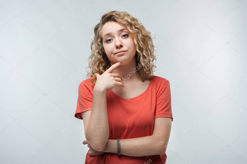 Image of nice brooding woman with curly hair thinking and looking aside, dressed in casual t-shirt. Human emotions, facial expression concept. Studio shot, white background