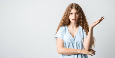What the hell are you talking about, nonsense. Studio shot of frustrated female with curly long hairstyle gesturing with raised palm, frowning, being displeased and confused with dumb question.